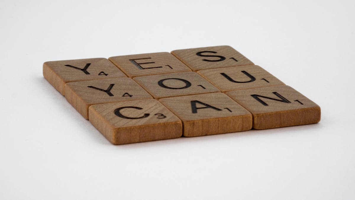 Wooden Scrabble tiles spelling 'Yes You Can' on a white background.